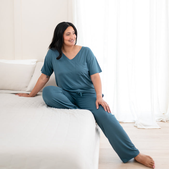 Female model sitting on a bed wearing the Womenβs Relaxed Fit V-Neck in Atlantic with matching women's lounge pants