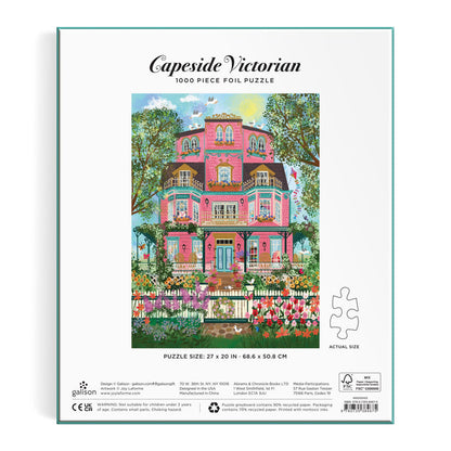 Back of the Joy Laforme Capeside Victorian 1000 Piece Foil Puzzle box features a vibrant illustration of a pink Victorian mansion with balconies, lush trees, and a white picket fence with flowers. Brand: Joy Laforme.