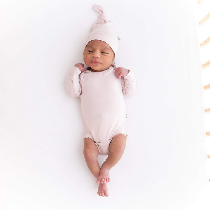 Newborn wearing Kyte Baby Long Sleeve Bodysuit in Blush with matching Knotted Cap